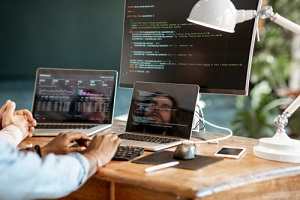 programmers writing a program code sitting at the workplace with three monitors in the office